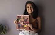 A smiling Latinx woman holds up a cookbook.
