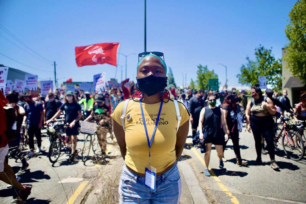 An image of an African American woman with short, blue hair standing in front of a group of marchers during a Juneteenth event.