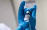 An image of a hand in blue gloves holding a vial of the COVID-19 vaccine.