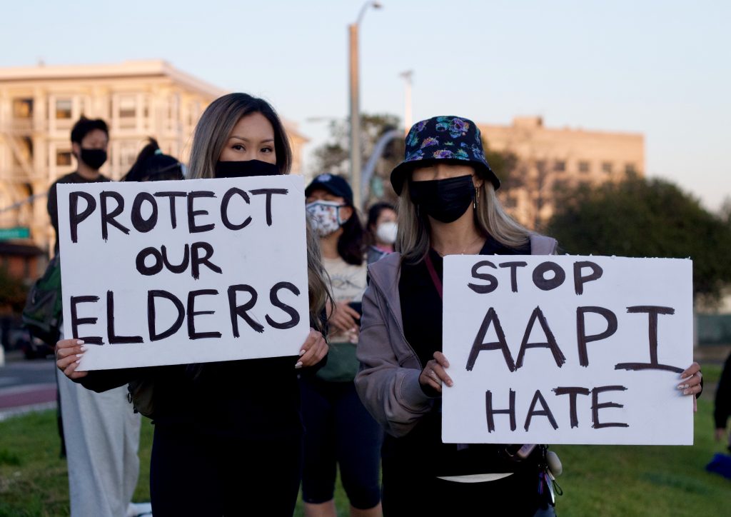 Two Asian American women wear face masks and hold signs that say "Protect our Elders" and "Stop AAPI Hate"