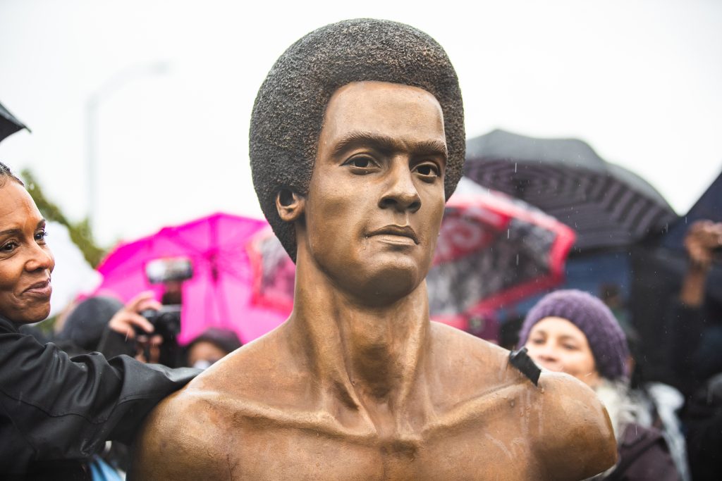 a bronze statue of a man with an afro smiling.