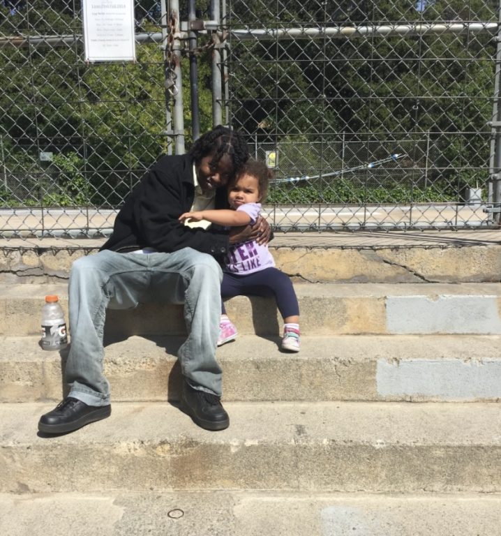 A Black woman hugs a biracial child on the steps at a public park