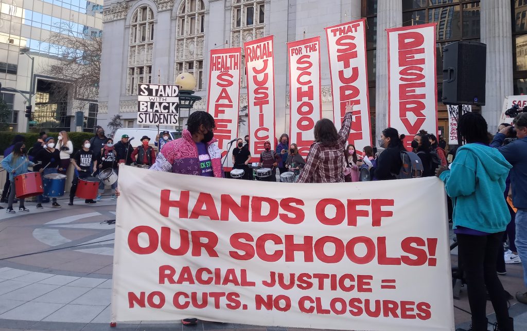 A banner that says "hands off our schools" in bold red letters in front of Oakland City Hall