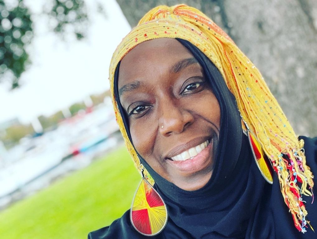 A Black woman smiles in a selfie wearing a bright yellow head scarf