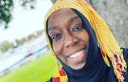 A Black woman smiles in a selfie wearing a bright yellow head scarf