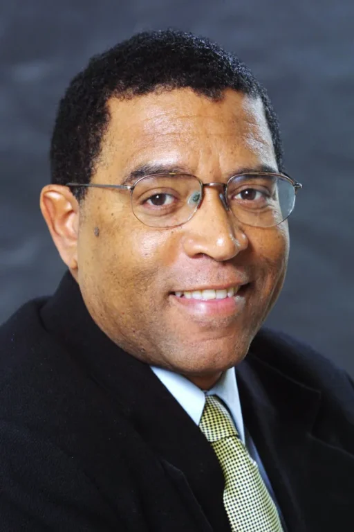 A black man wearing glasses smiles for a photo