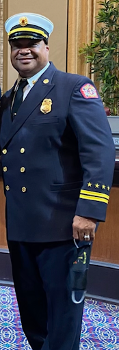 An African American man stands wearing a navy blue uniform